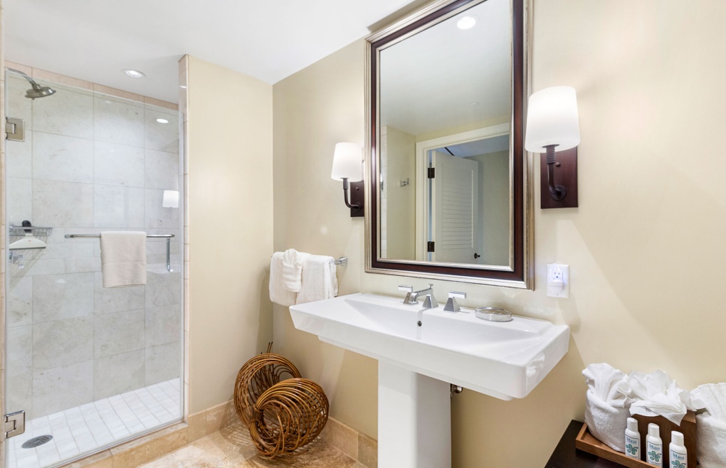 The guest bathroom offers a granite vanity with a glass and travertine walk-in shower